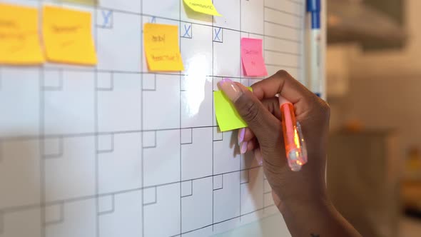 Crop black woman taking notes in planner on fridge