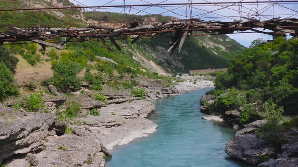 Aerial of woman balancing and walking on dangerous wooden bridge over fresh flowing Vjosa river amid