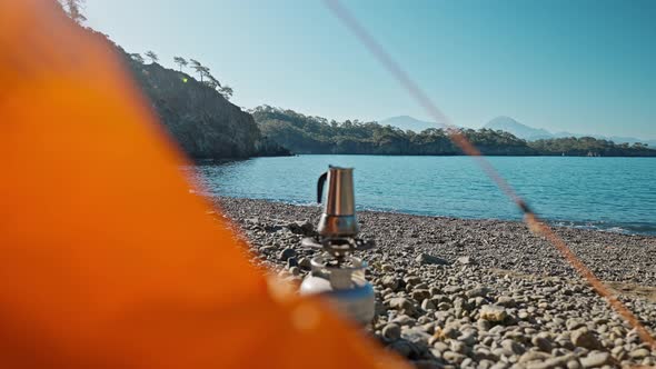 Orange Tent and Coffee Pot on Gas Stove on Wild Empty Pebble Beach at Morning on Coast of