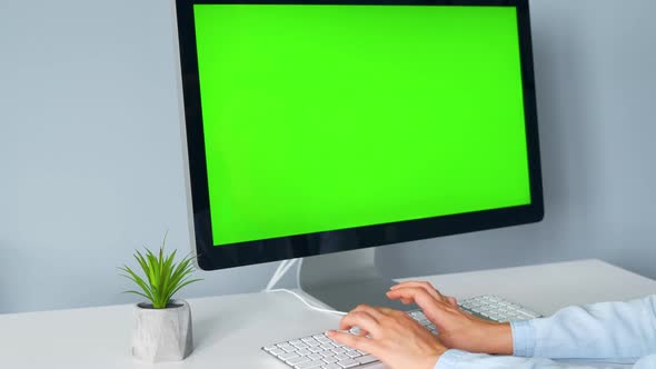 Woman Typing on a Computer Keyboard, Monitor with a Green Screen. Chroma Key. Copy Space