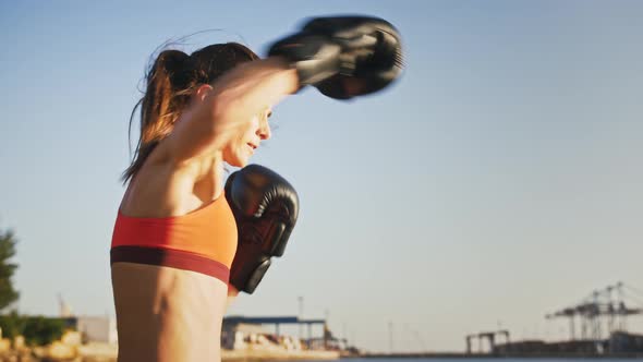 Young Hardy Woman in Leather Boxing Gloves and Sportswear is Boxing While Practicing By Seaside