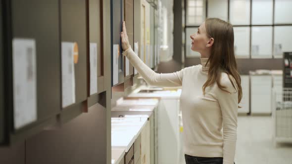 Young Woman in Shop Choosing Material for Facades for Kitchen Furniture