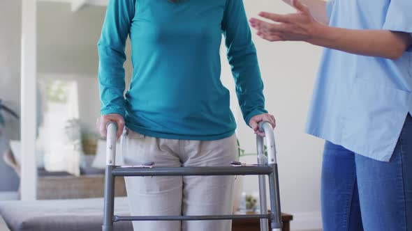 Female health worker assisting senior woman to walk with walking frame at home