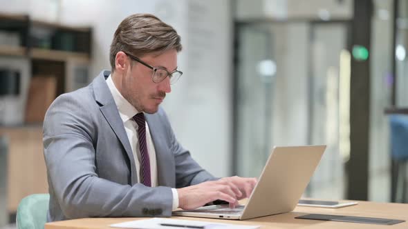 Pensive Businessman Thinking and Working on Laptop in Office