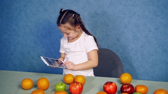 Girl using tablet at table, Portrait of little girl using tablet at table with fruits