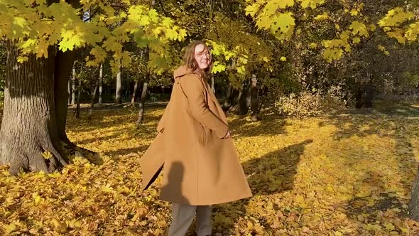 Happy woman in a coat dances and spins in the sunny autumn forest