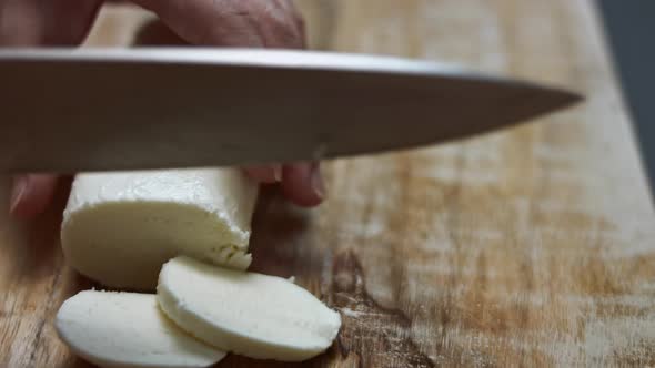 Female Hands Slicing Mozzarella Cheese on a Wooden Cutting Board