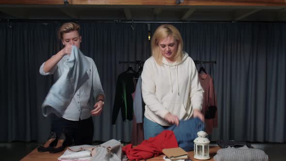 Young Women Second Hand Shop Workers Sort Clothes on Table