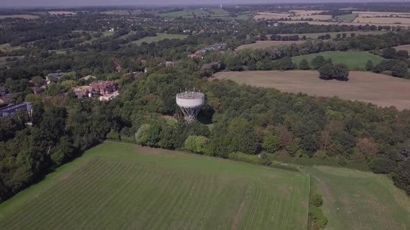 Drone aerial view orbiting water tower in Trent Park North London UK. Big vast green field rural tow