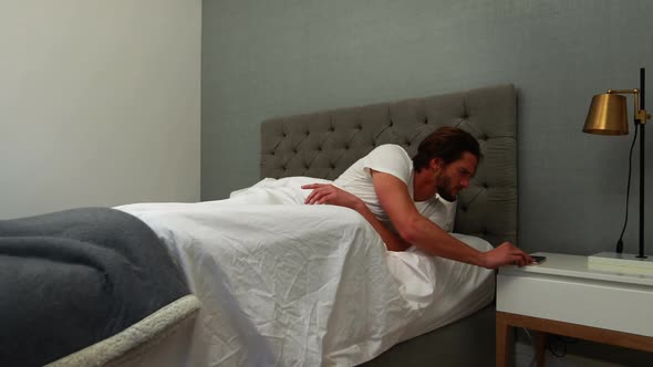 Young man waking up in bed and stretching his arms