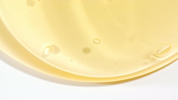 Macro Shot of Transparent Yellow Cosmetic Fluid Gel Cream With Bubbles Flowing Down on a White