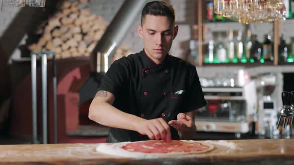 Chef Putting Slices of Sausage on Pizza Base