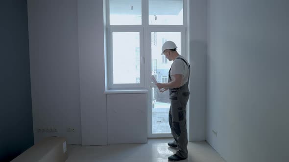 A Builder in Uniform Checks the Size and Quality of Window Installation in a New Apartment