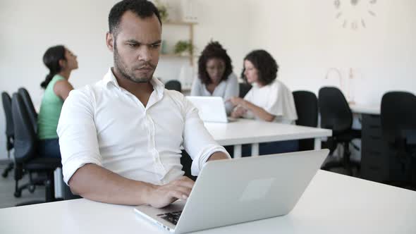 Pensive Office Worker Sitting at Table and Using Laptop