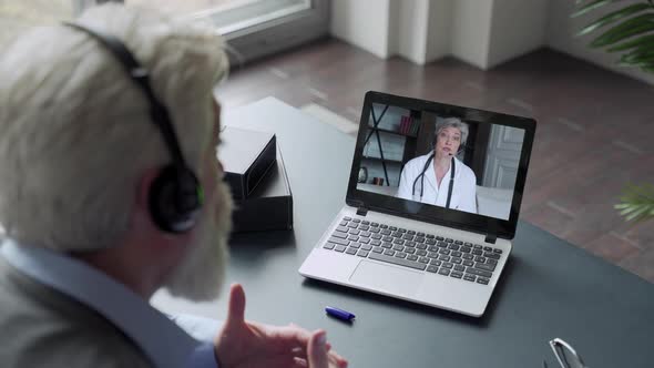 An Elderly Man with a Beard Communicates Via Computer with a Doctor Via Video Link. Medical Care in