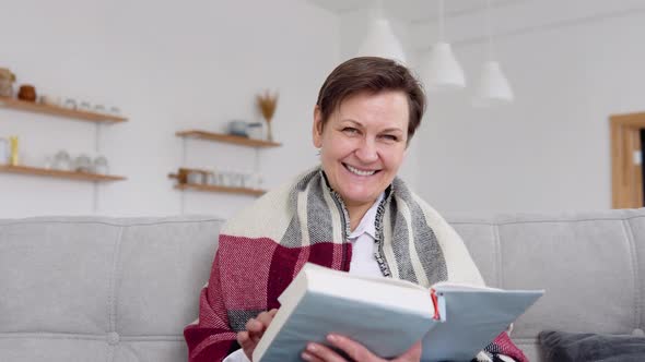 Senior Woman Reading a Book While Sitting on the Couch at Home