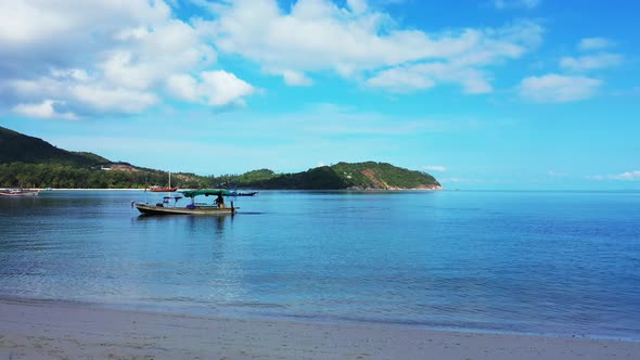 Fishing boat anchoring on calm lagoon washing sandy beach of tropical island, bright blue sky with w