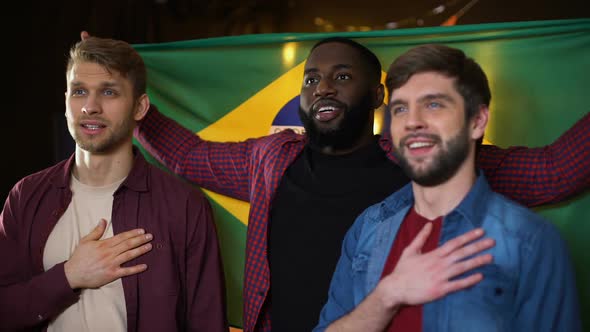 Brazilian Multiracial Football Fans Singing National Anthem, Waving Flag in Pub