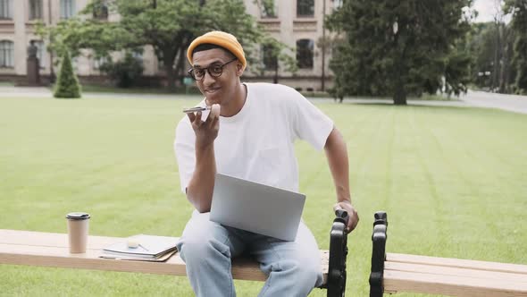 Young African American Student Sitting and Studying in the Campus Talking on the Phone with a Smile