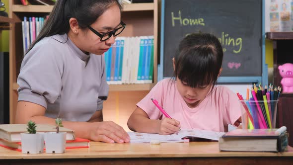 Asian little girl studies at home during quarantine with her mother. alt