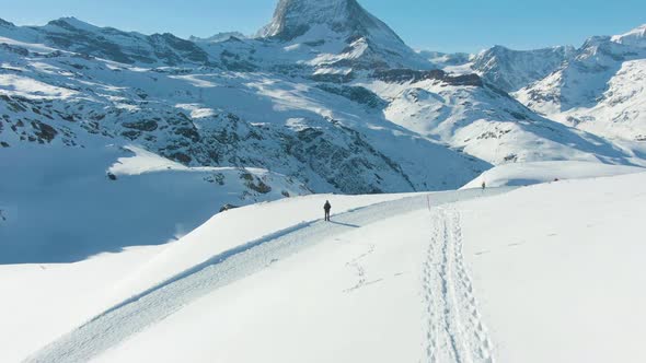 Blue Matterhorn Mountain in Winter Day and Hiker Man. Switzerland. Aerial View. Reveal Shot