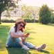 A Young Woman Uses Her Phone While Sitting on a Green Bright Lawn - VideoHive Item for Sale