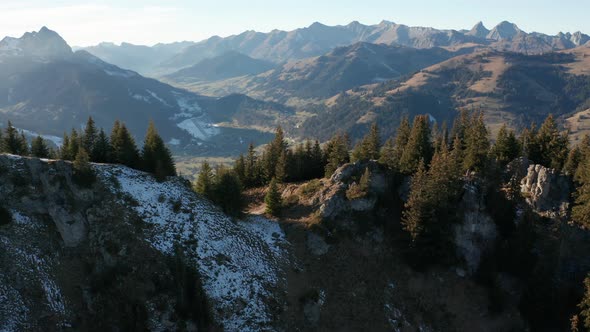 Jib down of mountain top with trees with large mountains in the background