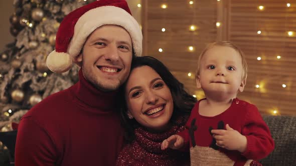 Portrait of Happy Young Family Sitting Together on Sofa In Lounge at Home on Christmas Day, Smiling