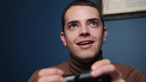 Happy Excited Young Caucasian Man Gamer Holding Controller Playing Video Games Sitting on Sofa