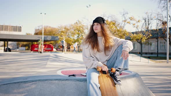 Street Girl with a Skateboard Wearing a Knitted Hat and Headphones