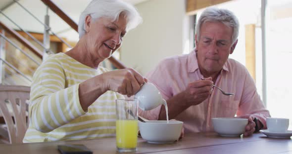 Senior caucasian couple pouring milk in cereal bowl having breakfast together at home