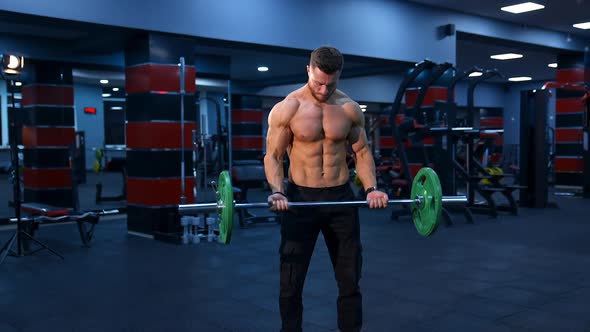 Male athlete with strong body and naked torso lifts barbell in modern gym. Slow motion.