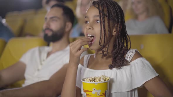 Pretty African American Girl Eating Popcorn in Cinema and Showing Thumb Up, Portrait of Happy Child