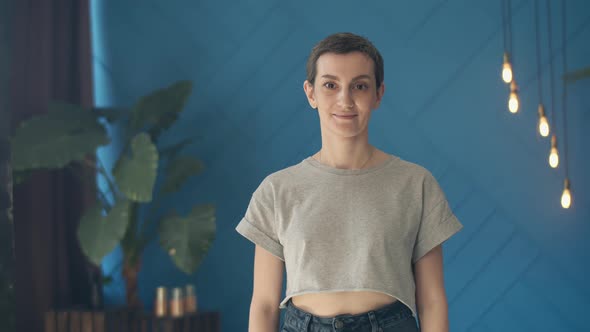 Cute woman with short hair is standing in the room looking at the camera and smiling, crossing arms