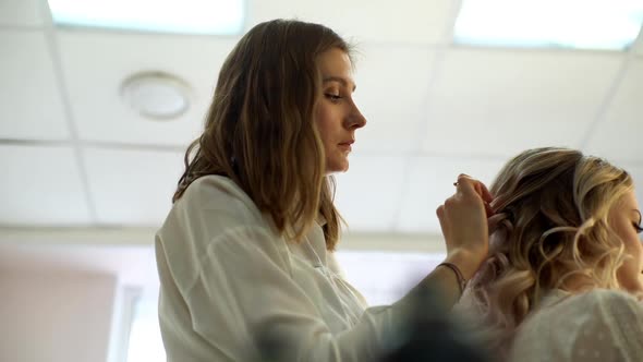 Stylist Hairdresser Combing Long Curls of Young Woman with Hand