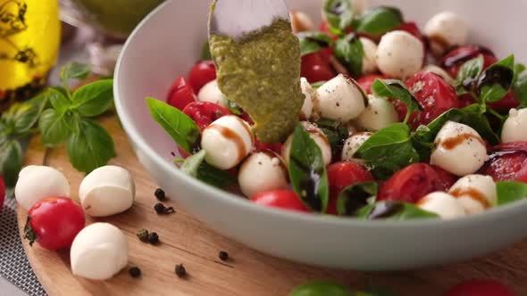 Pouring Pesto Sauce on Caprese Salad with Cherry Tomatoes and Mozzarella Cheese Balls