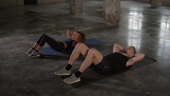 Young Stylish Man and Woman in Sportswear Workouting at Empty Studio Doing Synchronous Crunches