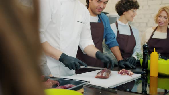 Tilt-up of Professional Cook Preparing Meat Dish in Cooking Class with Cheerful Students