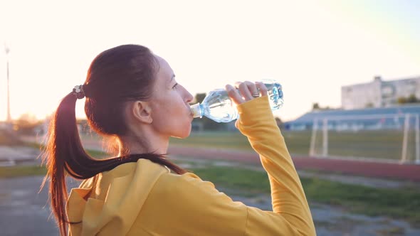 Fitness Young Woman Drinking From Sport Bottle During a Workout Pause in Stadium