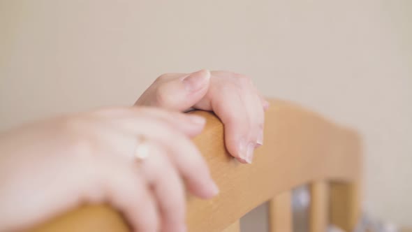 Mother Rocks Gently Wooden Crib at Beige Wall Closeup