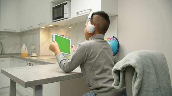 Rear View of Black Preteen Kid Playing Video Game on Tablet at Home