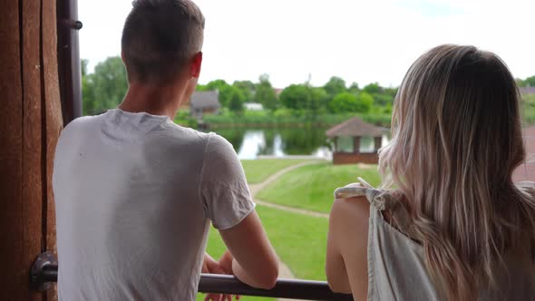 Back View Young Loving Couple Leaning on Handrails Standing on Terrace Talking Pointing Away in Slow