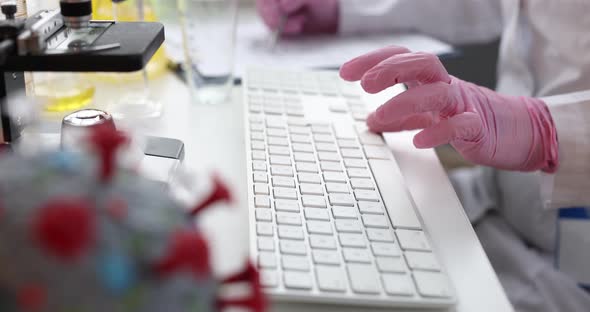 Scientist in Gloves is Typing a Mockup of Virus on Keyboard on Table Closeup