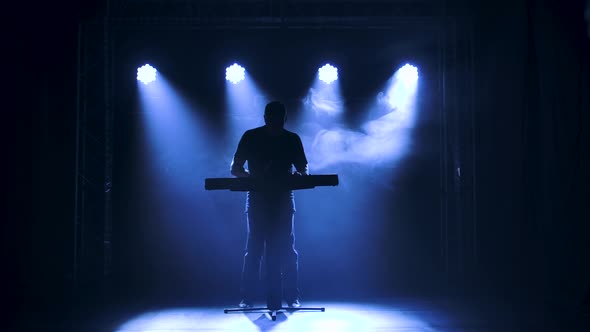 Musician Silhouette Playing on Synthesizer Piano Keyboard on Stage in a Dark Studio with Smoke and