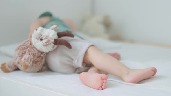 Barefoot Legs of Toddler Baby Lying on Bed with Fluffy Goat in Hands Sleeping