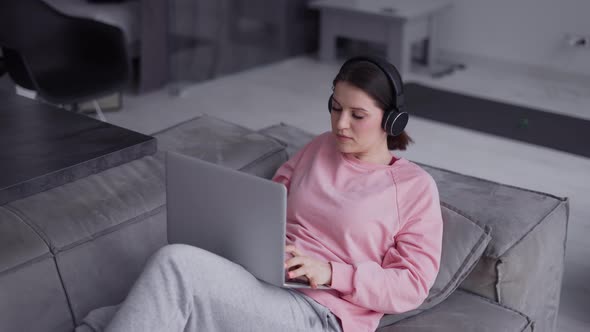 Woman Working with Laptop Computer and Listening Music By Headphone on a Couch