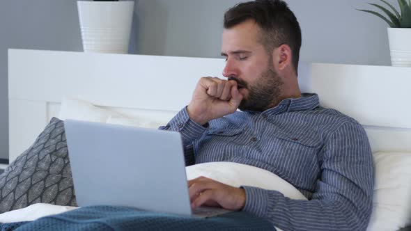 Sick Man Coughing while Using Laptop, Lying in Bed