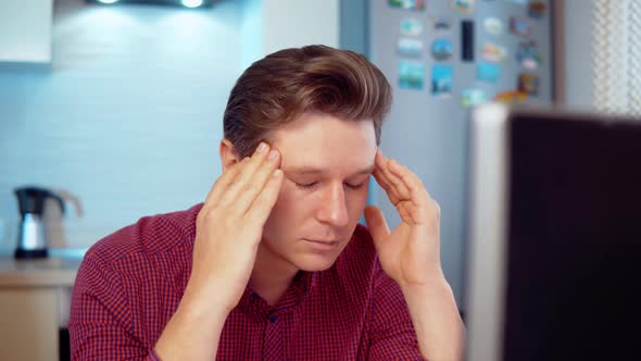 A Man at a Computer Massages His Head From Fatigue