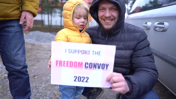 Portrait of a Man in a Warm Jacket with a Small Son Holding a Poster I Support Freedom Convoy 2022