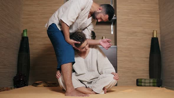 Male Thai Massagist is Massaging Young Woman's Neck with His Elbow Standing Nearby Her